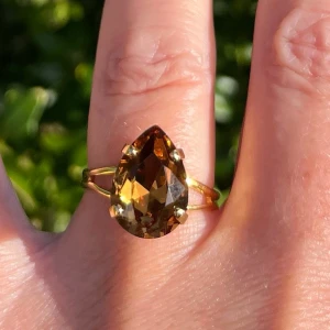 Ring Pear kristall  - Ring i guldpläterad mässing med kristall. Pear kristall 14x10mm, Smoked Topaz. Ställbar storlek. De sista bilderna visar andra färger och modeller som finns i lager.  Jag skickar endast spårbart, samfraktar. Fast pris. Besök gärna mina övriga annonser.  Till mina smycken använder jag kristaller från Preciosa, Aurora och Swarowski.