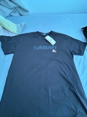 Svart Burberry t-shirt - Säljer en svart t-shirt från Burberry i mjuk bomull. T-shirten har korta ärmar, rund halsringning och Burberry-logga tryckt på bröstet tillsammans med det klassiska Burberry-emblemet. Perfekt för en clean och stilren look. storlek M till båda bytt med prislapp