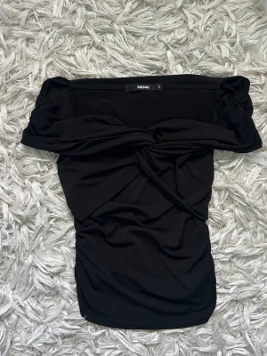 Svart offshoulder topp från BikBok - Fin svart off shoulder topp från BikBok med twistad detalj framtill. Är gjord i ett mjukt stretchigt material. Bild 3 är lånad från en annan användare på plick som sålde en likadan topp!