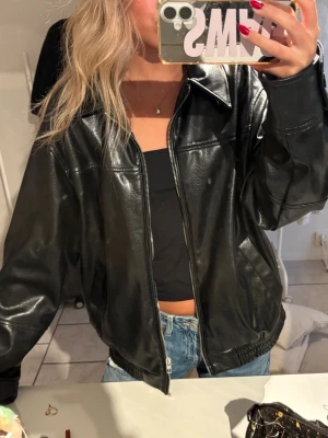 Svart oversized skinnjacka från ZARA - Snygg svart oversized skinnjacka med dragkedja framtill och bred krage. Jackan har en avslappnad passform och resår vid midjan för en cool look.