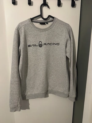 Grå sweatshirt från Sail Racing - (Priset kan ändras och diskuteras) Snygg grå sweatshirt från Sail Racing med svart logotyptryck på bröstet. Tröjan har rund halsringning, långa ärmar och ribbade muddar vid ärmslut och nederkant. Perfekt för en avslappnad och sportig stil. Har ni frågor hör gärna av er😃
