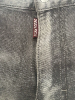Grå slitna jeans från Dsquared2 - Säljer ett par grå jeans från Dsquared2 med slitningar och hål på låret för en cool, avslappnad look. Jeansen har klassisk femficksmodell och raka ben. Perfekta för dig som gillar streetwear och vill sticka ut lite extra.