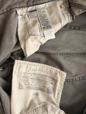 Grå Levi's 501 jeans - Säljer ett par klassiska grå Levi's 501 jeans med raka ben och knappgylf. Jeansen är tillverkade i bomull och har den ikoniska innerficksetiketten. Perfekta för en avslappnad och tidlös stil.