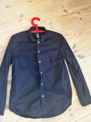 Ralph Lauren skjorta  -  Mörkblå skjorta ifrån Ralph Lauren i bra skick. Storleken är large i junior, vilket motsvarar XXS till XS. Nypriset är 1200. Men jag säljer den för 300. tveka inte att höra av dig vid minsta fundering.