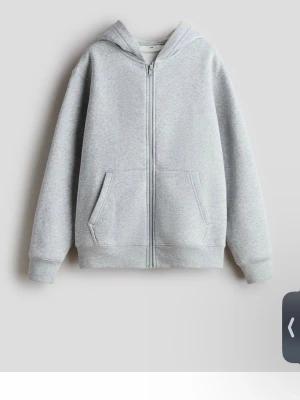 Ljusgrå zip hoodie med huva - En stilren ljusgrå hoodie med dragkedja framtill och två fickor. Hoodien har en klassisk huva och ribbade muddar vid ärmar och nederkant. Perfekt för en avslappnad look och enkel att matcha med andra plagg.