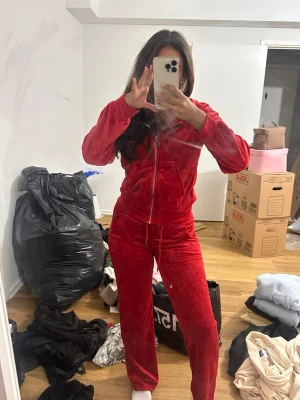 Röd velour loungewear-set lager 157  - Mysigt rött loungewear-set i velour med dragkedja framtill och huva. Setet består av en zip-hoodie och matchande byxor med resår i midjan och dragsko. Perfekt för chill dagar hemma eller när du vill vara extra bekväm. Byxor storlek xs och Tröja i s 