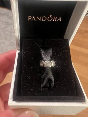 Pandora silverring med hjärtan - Fin berlock från Pandora i silverfärg med hjärtformade detaljer, där varje hjärta har en glittrande sten i mitten. Perfekt att använda på armband eller halsband för att ge din stil en personlig touch.