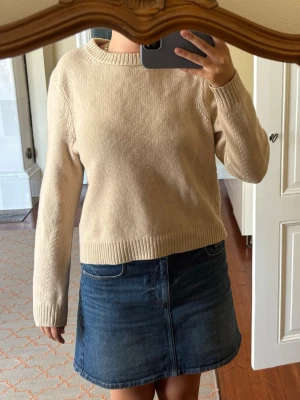 Beige stickad tröja med rund hals - En enkel och stilren beige stickad tröja med rund halsringning och långa ärmar från Filippa K. Tröjan har ribbade muddar vid ärmslut och nederkant, vilket ger en klassisk look. Och snyggt mönster längs armarna! Perfekt att matcha med jeans eller kjol för en avslappnad stil. Använd några gånger men fortfarande i ett gott skick