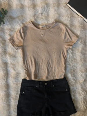 Ljusbeige basic t-shirt - En enkel och stilren ljusbeige t-shirt med rund hals och korta ärmar. Perfekt till jeans eller shorts för en clean och avslappnad look. Tillverkad i mjuk bomull som känns skön mot huden.