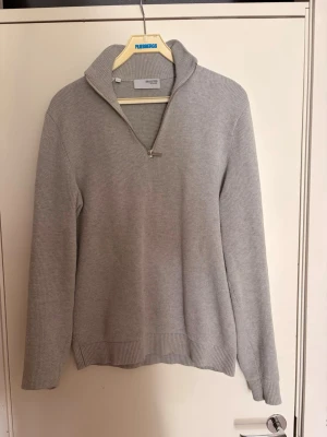 Selected home half zip - Snygg ljusgrå stickad tröja från selected home med halvzip och hög krage. Tröjan har långa ärmar och ribbade muddar vid ärmslut och nederkant. Perfekt för lager på lager och enkel att matcha med olika outfits.