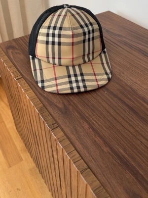 Burberry keps  - Snygg burberry keps i klassiskt beige rutigt mönster. Kepsen har svart mesh på sidorna och bak, samt böjd skärm. Perfekt för dig som vill ha en trendig och tidlös accessoar till din outfit. Använd ett få tal gånger då produkten är i bra skick och nästan som ny. 