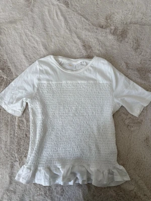 Vit tshirt Gina  - Säljer denna superfina tshirt med volang från Gina Young, i storlek 158/164. Den är använd få gånger o därför i mycket bra skick!