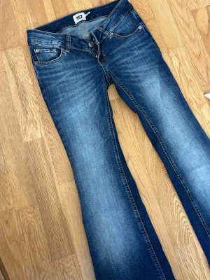 Blå bootcut jeans från 157 - Säljer ett par klassiska blå bootcut jeans från 157 med snygga slitningar och kontrastsömmar. Jeansen har fem fickor och normal passform i midjan. Perfekta till sneakers eller boots för en avslappnad look.