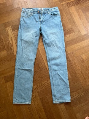 Ljusblå raka jeans - Säljer ett par ljusblå jeans med rak passform och klassisk femficksdesign. Jeansen har normal midja och stängs med dragkedja och knapp. Tillverkade i denim med en avslappnad look, perfekta till vardagsstilen. Jeansen är regular fit och är använd ett fåtal gånger och ser ut som helt ny.