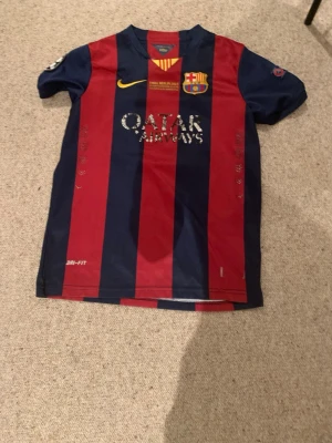 FC Barcelona Messi matchtröja - Säljer en klassisk FC Barcelona matchtröja med Messi 10 på ryggen. Tröjan har breda blå och röda ränder, klubbmärke och Nike-logga på bröstet samt Qatar Airways som sponsor. Tillverkad i lätt och ventilerande Dri-FIT-material. Passar 12 till 13 åringar