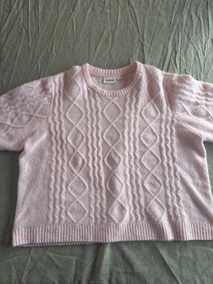 Ljusrosa tröja Kappahl - Supersöt ljusrosa tröja från Kappahl. Tröjan har ett klassiskt flätmönster framtill och baktill, rund halsringning och ribbade muddar.