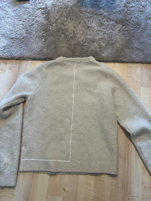 Beige stickad tröja från Zara - Säljer en beige stickad tröja från Zara med minimalistisk design. Tröjan har en rak passform, ribbade muddar och en dekorativ söm på ryggen. Perfekt för dig som gillar stilrena plagg i mjukt material. Lite nopprig men jag noppar av den innan ja skickar! Tar alla bud! Lite. I storlek!!