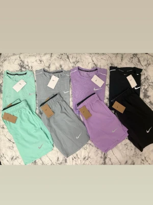 Nike shorts i mint, grå, lila & svart - Säljer 4 st helt nya Nike Miller set i storlek M. Alla är oanvända och har tags kvar och säljs endast i set, alltså T-shirt + shorts tillsammans. Materialet är väldigt lätt, luftigt och skönt, perfekt för gym, löpning, promenader eller vardag. Storleken är M, men de kan även passa dig som brukar ha S beroende på hur du vill att de ska sitta. Snygg passform, passar de flesta och är riktigt bekväma att använda. Helt nya med tags kvar och säljs som kompletta set (T-shirt + shorts). 499kr/st (set). 