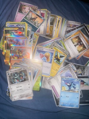 112st Vanliga pokemonkort - Säljer en blandad samling Pokémonkort med olika typer, färger och motiv. Här finns både vanliga och holografiska kort, med allt från klassiska till nyare Pokémon. Perfekt för dig som vill bygga din lek eller utöka din samling. Korten är av papper och har färgstarka illustrationer.