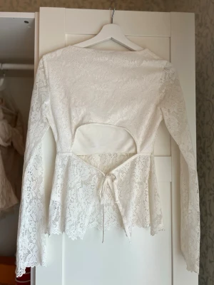 Vit spetsblus - öppen rygg - Säljer en vit långärmad spetsblus med snygg öppen rygg och snörning i midjan. Mycket bra skick använd ca 2 ggr🤩🤩