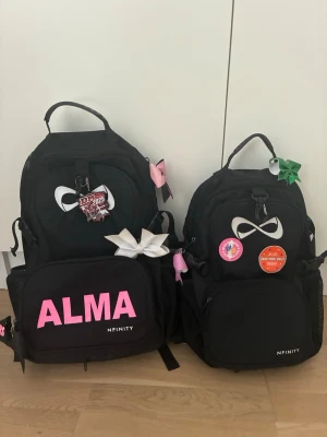 Nfinity cheer väska - Säljer två svarta väskorfrån Nfinity. Den lilla i bättre skick. Den stora med texten Alma på går det att ta av texten. Org pris för den stora ca 1700 och den lilla ca 1200. Den stora säljs för 900kr och den lilla för 700kr. Tillsammans för 1500.