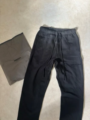 Svarta Essentials mjukisbyxor - Säljer ett par svarta mjukisbyxor från Essentials Fear of God. Perfekta för en avslappnad och trendig look. Storlek L, ej använda
