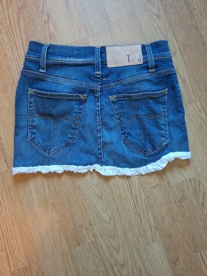 Blå jeanskjol med volangkant (egenjord) för kort barn - Jag säljer denna blåa jeanskjolen det var orginalt ett par jeans jag hade när jag var runt 7-9 nu är jag 14 o 160 och den passar i storlek fast är lite kort på mig fast skulle passa fint på ett litet barn. Bra skick fast är gjord av mig så inte den bästa i stygnen