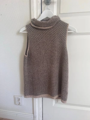 Stickad ärmlös brun polotröja - Snygg ärmlös stickad tröja i brunt och beige med polokrage. 34% ull. Köpt secondhand, märket är Liz Claiborne Collection. 