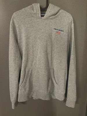 Grå hoodie från Polo Sport - Tja! Jag säljer en snygg grå hoodie från Polo Sport Ralph Lauren med broderad logga och amerikansk flagga på bröstet. Klassisk känguruficka framtill och huva. Tillverkad i mjuk bomullsblandning som är perfekt för chill dagar. Det är storlek Xs/S på den fast det står XL/18-20, Det är bara att hojta till vid någon fundering:)