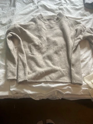 Beige stickad tröja med rund hals - Mysig beige stickad tröja med rund halsringning och långa ärmar. Tröjan har en enkel och stilren design med ribbstickade muddar vid halsen. Perfekt för lager på lager och passar till det mesta i garderoben.