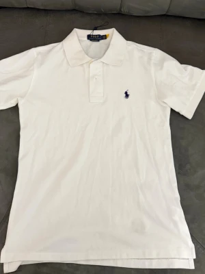 Ralph Lauren - Klassisk vit pikétröja från Polo Ralph Lauren. Tröjan har Krage och knappar framtill, perfekt till jeans eller shorts för en clean look.