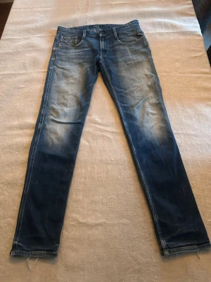 Replay jeans - Snygga blå jeans med slitningar och tvättade detaljer på låren och knäna. Klassisk femficksmodell med normal midja och dragkedja. Jeansen har råa kanter vid bensluten för en trendig look. Perfekta för dig som gillar en avslappnad men stilren stil. Storlek: W30L32 Modell: ingen aning 