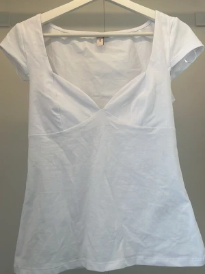 Vit croppad topp  (den är helt ny) - Snygg vit croppad topp med djup v-ringning och korta ärmar. Toppen har en figurnära passform och markerad byst, vilket ger en modern och fräsch look. Perfekt att matcha med både jeans och kjol för en trendig outfit.