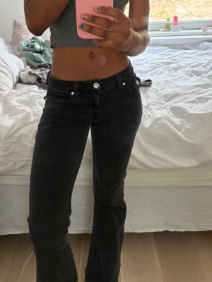 Svarta bootcut jeans med låg midja - Säljer ett par svarta bootcut jeans med låg midja och klassisk femficksmodell. Jeansen har raka ben med lätt utsvängning nedtill och silverfärgade knappar. Perfekta till en trendig och avslappnad look.