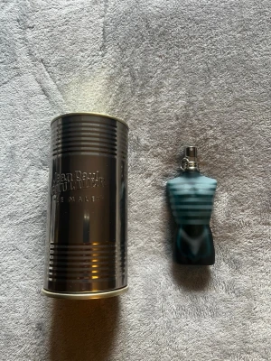 Jean Paul Gaultier Le Male parfym - Klassisk parfym från Jean Paul Gaultier, Le Male, med en ikonisk flaska formad som en manlig torso i blått frostat glas. Kommer med original metallburk som har präglad logga. Flaskan har silverfärgad spraykork och en unik design som sticker ut i badrumsskåpet.
