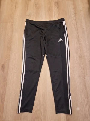 Adidas Träningsbyxor (Svart/Vit) – Stl M ⚽ - Klassiska Adidas-träningsbyxor i svart med vita tre ränder! Sköna mjukisbyxor med elastisk midja, praktiska fickor och dragkedja vid bensluten. Perfekta för träning eller häng. Gott begagnat skick! ⚡📦