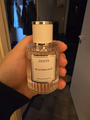 Zents Heartbreaker Extrait de Parfum - Zents Heartbreaker Extrait de Parfum i en elegant, genomskinlig glasflaska med räfflad design och vit etikett. Flaskan har ett vitt lock med silverdetaljer som ger en lyxig känsla. Perfekt för dig som vill ha en exklusiv doft i samlingen.