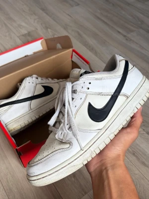 Nike dunks lows - Säljer ett par klassiska vita Nike sneakers med svart swoosh och vita skosnören. Skorna har lågt skaft och perforerad tåbox för extra ventilation. Yttermaterialet är i läder och sulan är vit med diskret mönster. Perfekta för en clean och sportig look.