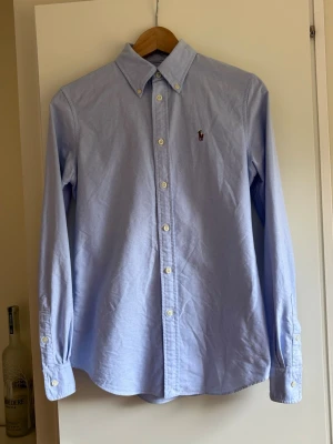 polo ralph lauren - Klassisk ljusblå skjorta från polo ralph lauren knappar hela vägen framtill och button-down krage. Skjortan har lång ärm och en liten broderad logga på bröstet. Tillverkad i bomull för en bekväm känsla och snygg passform.