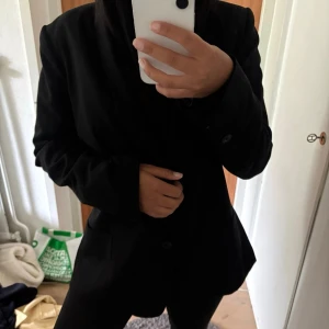 Svart kavaj från Gina Tricot - Stilren svart kavaj från Gina Tricot i klassisk rak modell. Kavajen har enkelknäppning, långa ärmar och är helfodrad för en snygg siluett. Perfekt att matcha med både jeans och kostymbyxor för en trendig look.