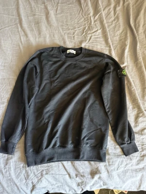Svart sweatshirt från Stone Island - Snygg svart sweatshirt från Stone Island med klassisk rund hals och ribbade muddar. Ikoniska Stone Island-loggan sitter på vänstra ärmen. Tillverkad i mjuk bomull för skön känsla och stilren look.