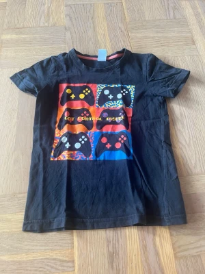 T-shirt - Svart t-shirt med färgglatt tryck av spelkontroller i storlek 128 