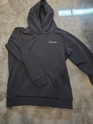 Svart hoodie från Peak Performance - Snygg svart hoodie från Peak Performance med klassisk logga på bröstet. Hoodien har en stor huva och en praktisk magficka. Tillverkad i mjukt material som känns skönt mot huden. Perfekt för en avslappnad och stilren look. Passar perfekt på dig som har storlek 170. Hör av dig om du har frågor😊