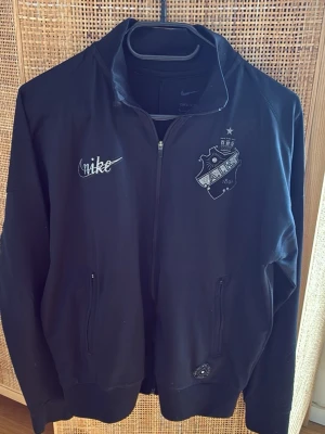 Nike Limited edition - AIK Smokinglirare jacka - Svart ziptröja med AIK-emblem på bröstet och Nike-logga. Två fickor med dragkedja framtill och texten 'SMOKINGLIRARE' samt '1891' broderat på ryggen. Perfekt för dig som vill representera AIK med stil. Liten i storlek, närmare S än M tycker jag.