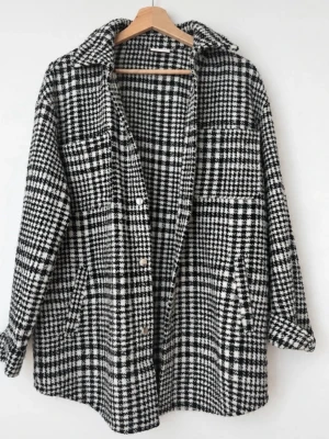 Overshirt/Jacka i svartvitt rutmönster från Vila - Stilren overshirt från Vila i svartvitt rutmönster. Jackan har klassisk krage, knäppning framtill och två bröstfickor. Materialet är tjockt och mjukt, perfekt för lager på lager. Passar dig som gillar trendiga och tidlösa plagg.