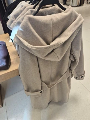 Beige kappa med huva från Zara - Stilren beige kappa med stor huva och knytskärp i midjan. Köpte för 799 men säljer för 529!!!