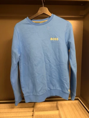 Blå sweatshirt från BOSS - Snygg blå sweatshirt från BOSS med rund halsringning och diskret BOSS-logga på bröstet. Tröjan har långa ärmar och ribbade muddar vid ärmslut och nederkant. Perfekt för en avslappnad och stilren look.