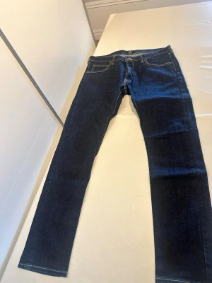 Mörkblå raka jeans från Lee - Snygga mörkblå jeans från Lee med raka ben och klassiska kontrastsömmar. Jeansen har fem fickor och en patch med Lee-loggan bak i midjan. Perfekta till en avslappnad stil och tillverkade i slitstarkt denimtyg.