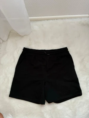 Svarta shorts med normal passform - Säljer ett par enkla svarta shorts med normal passform och elastisk midja. Perfekta till sommaren och tillverkade i mjukt bomullsmaterial. Klassisk design utan synliga detaljer eller mönster. Pris kan diskuteras vid snabb affär!