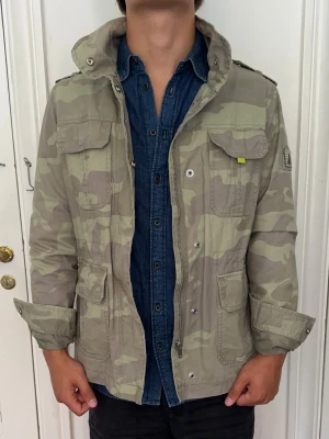 Field jacka camo - Snygg field jacka i camo från okänt märke. Dragkedja och knappar. Riktigt bra skick. Storlek FR42, skulle säga att den passar som medium